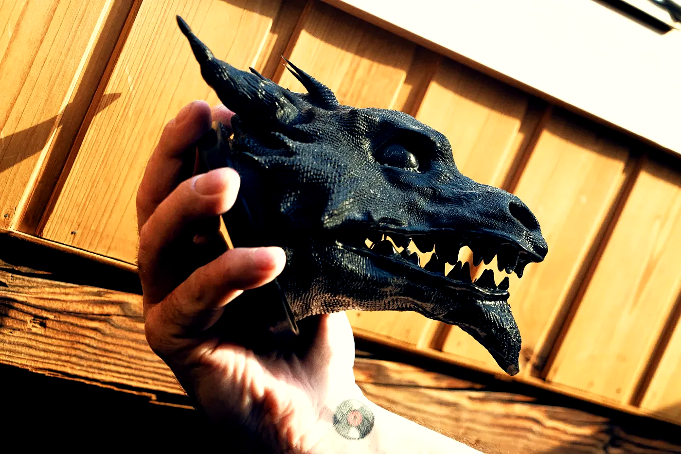 The finished Drachenkopf held in an open hand against wood: a horned dragon head in dark resin