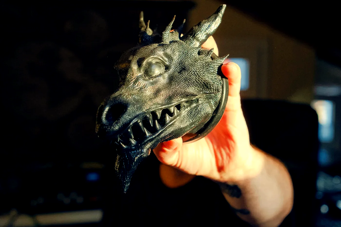 The finished Drachenkopf held in an open hand against wood: a horned dragon head in dark resin