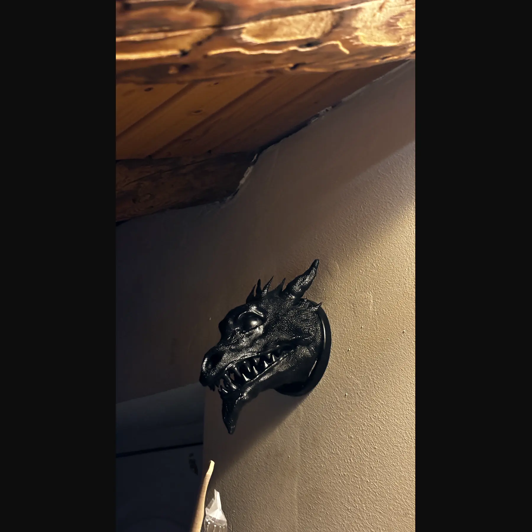 The finished Drachenkopf held in an open hand against wood: a horned dragon head in dark resin