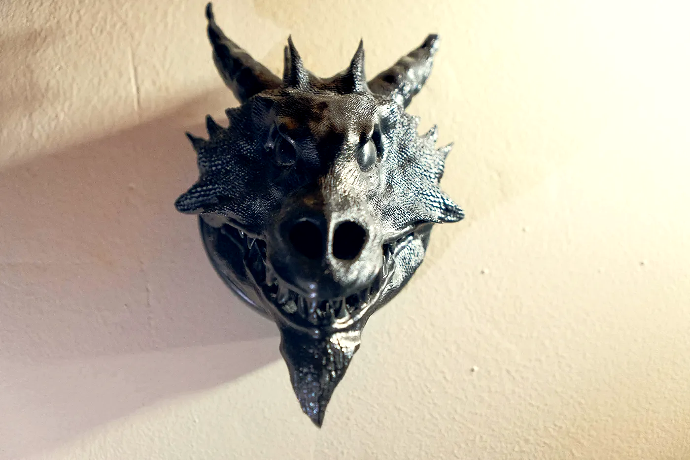 The finished Drachenkopf held in an open hand against wood: a horned dragon head in dark resin