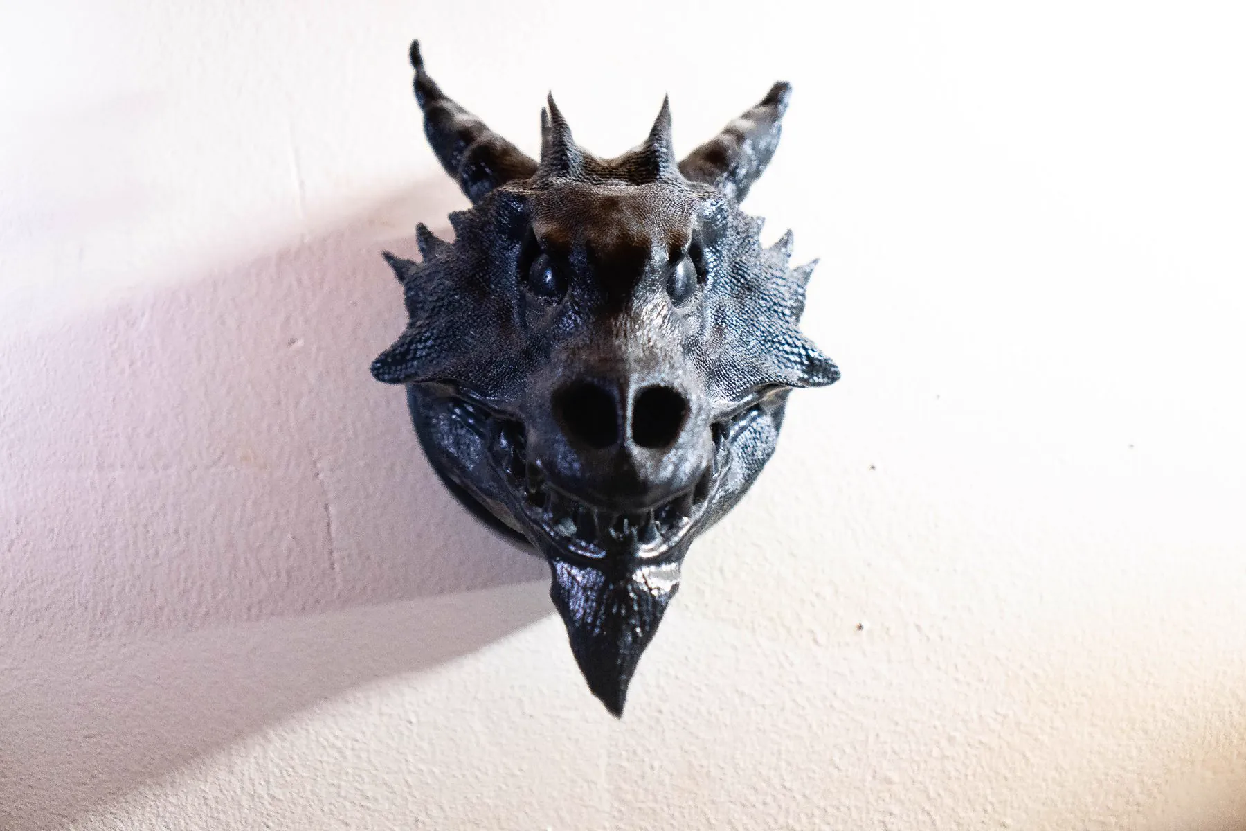 The finished Drachenkopf held in an open hand against wood: a horned dragon head in dark resin