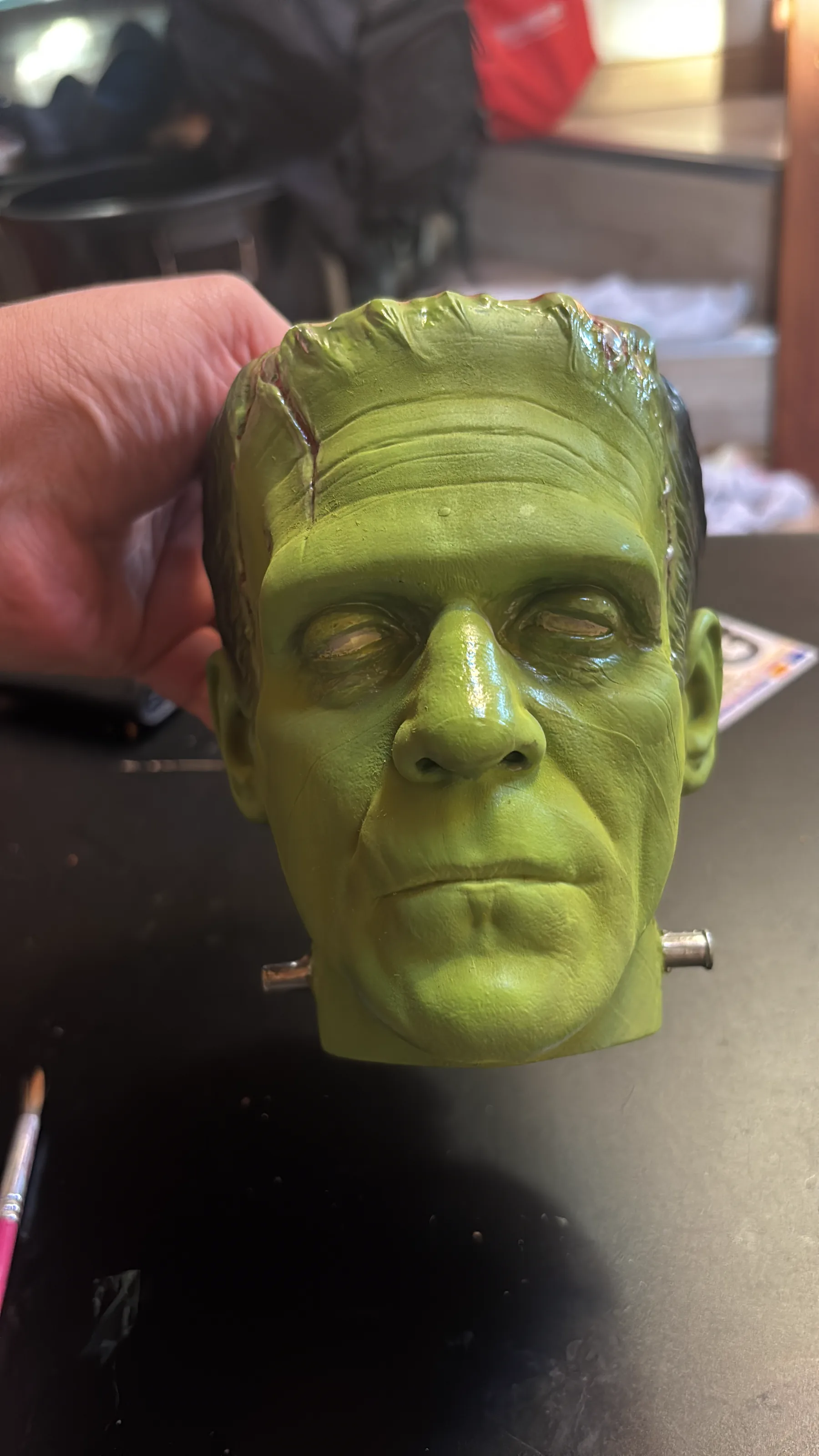 The Frankenstein cup rendered in 3D against black, seen face on, the stitches and bolts catching the light