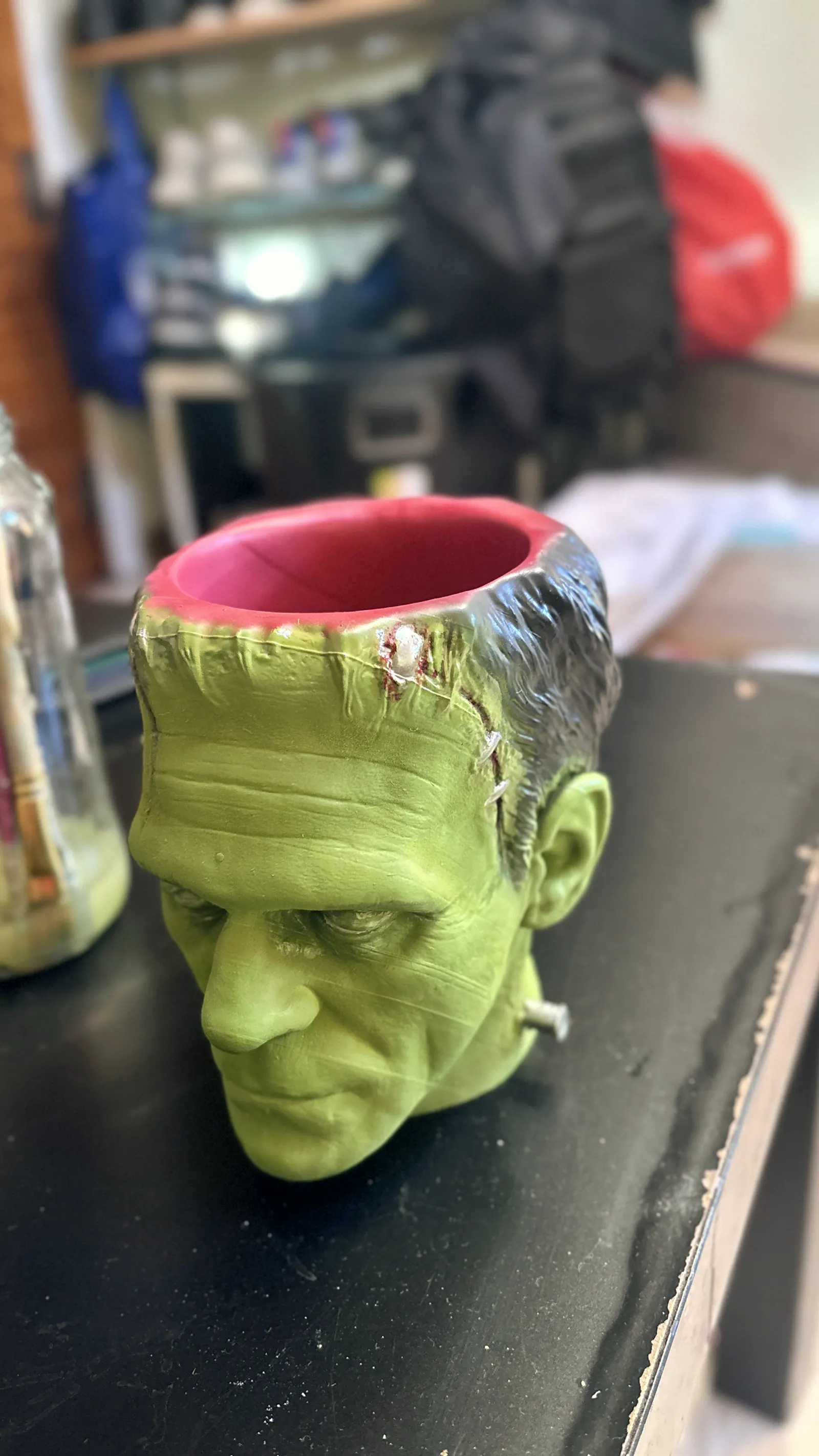The Frankenstein cup rendered in 3D against black, seen face on, the stitches and bolts catching the light