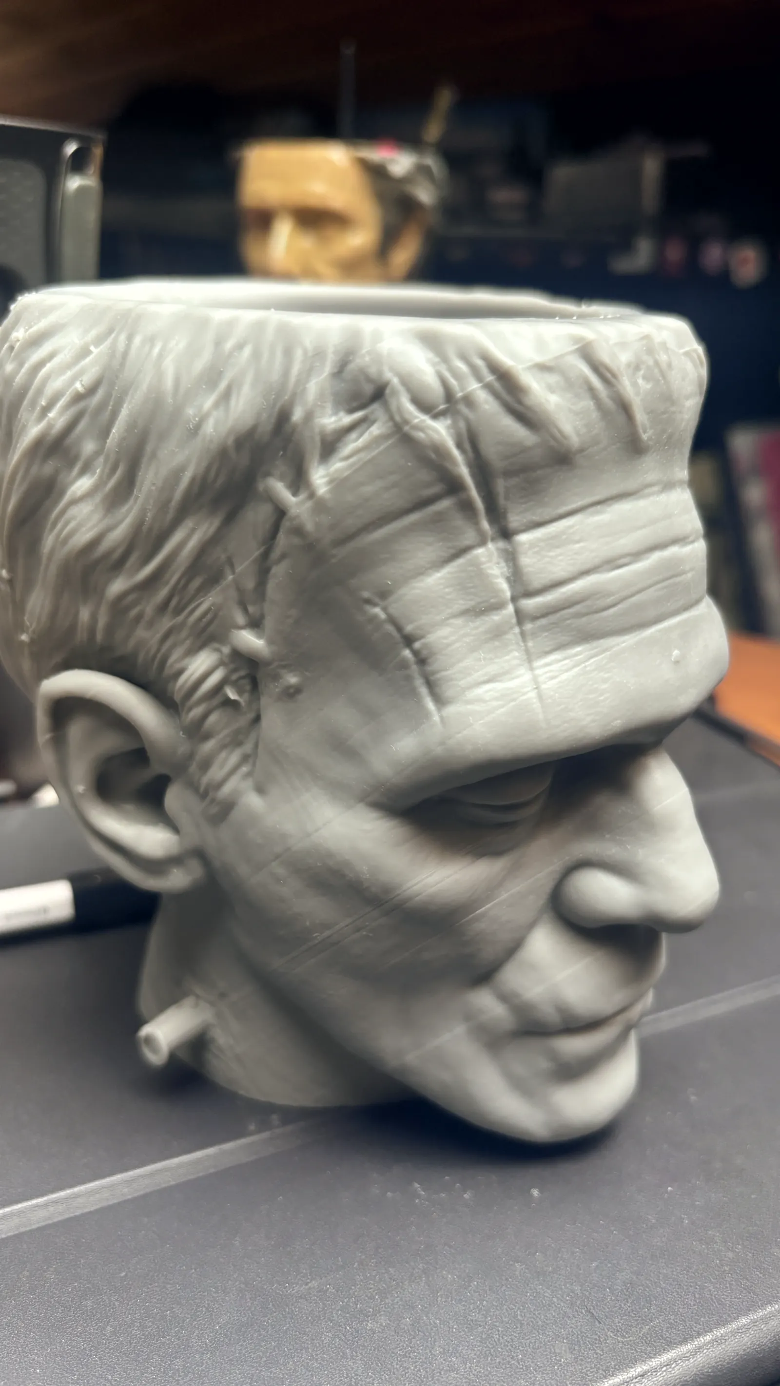 The Frankenstein cup rendered in 3D against black, seen face on, the stitches and bolts catching the light
