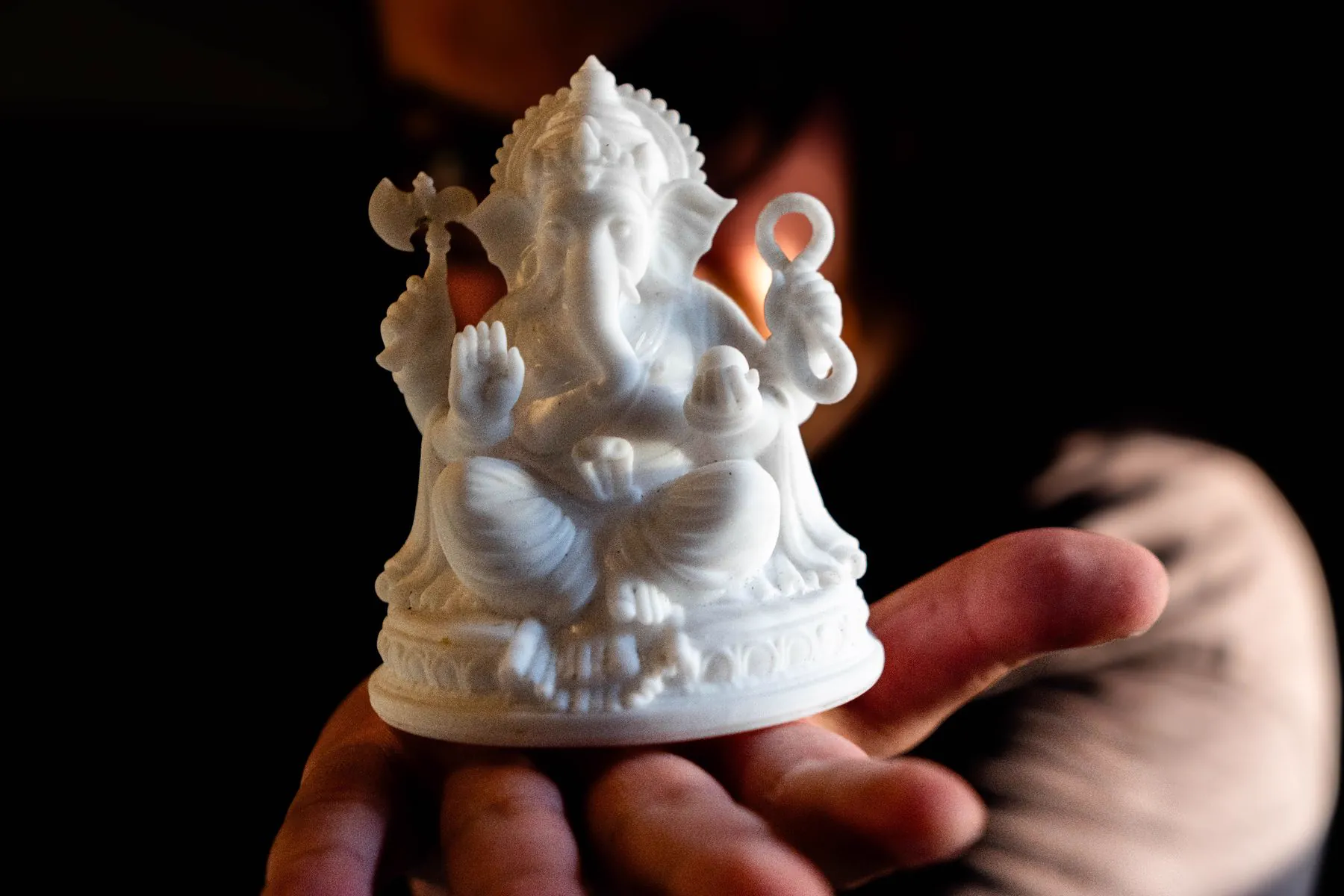 White resin Ganesha figure resting on an open palm against a dark background