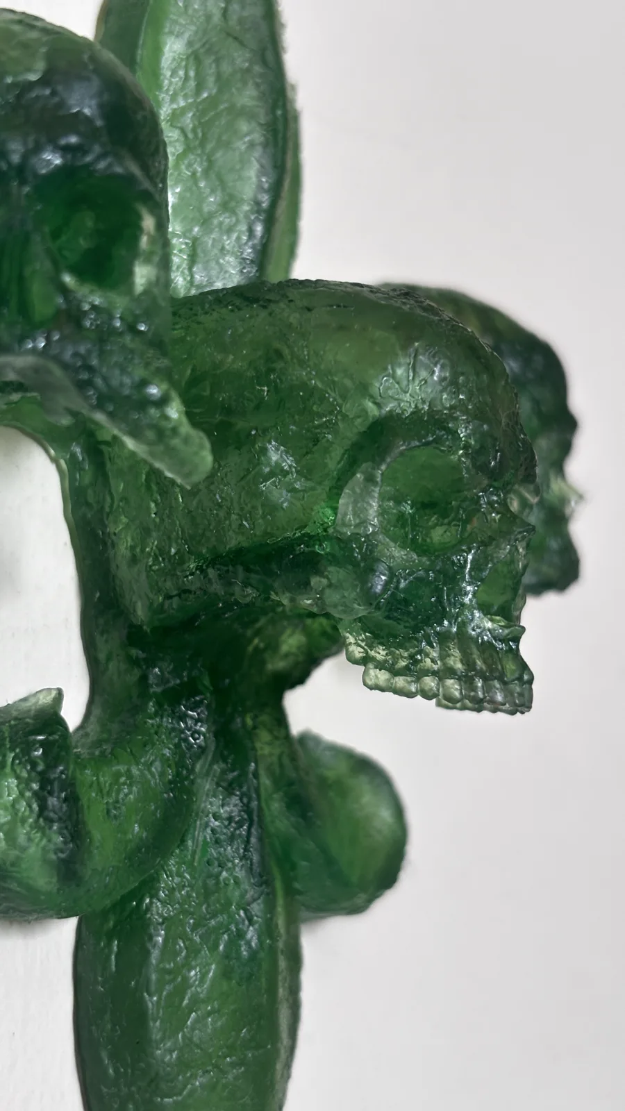 A fleur-de-lis built from skulls, cast in deep red translucent resin, mounted on a pale wall with its shadow beside it