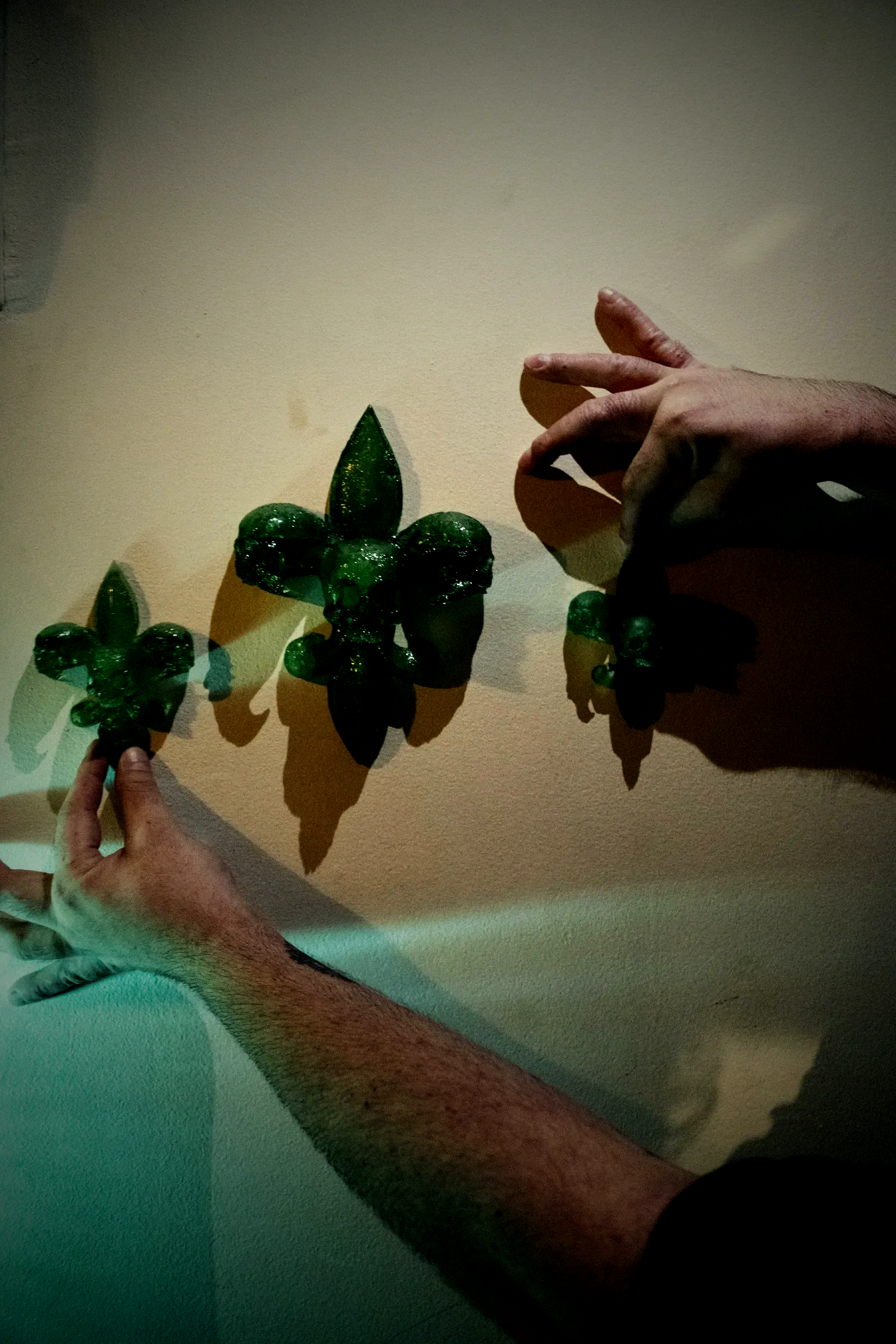 A fleur-de-lis built from skulls, cast in deep red translucent resin, mounted on a pale wall with its shadow beside it