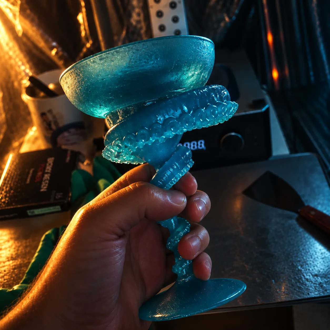 Translucent teal cocktail coupe held up in the hand, light passing through the sculpted tentacle stem